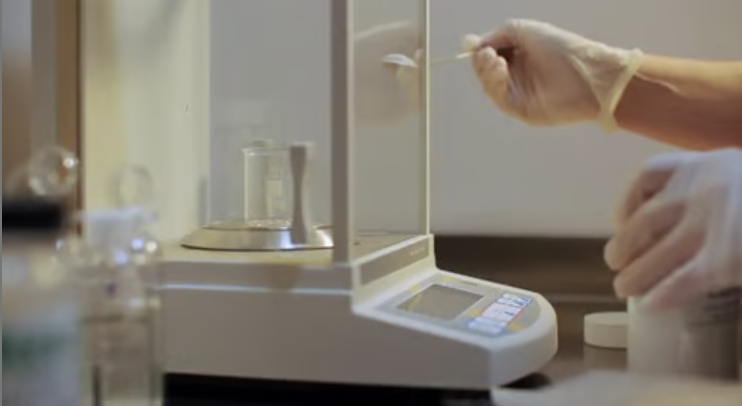 Human hand dosing powder on an analytical balance